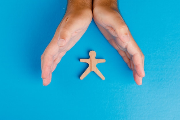 Free Photo social protection concept on blue table flat lay. hands taking care of wooden human figure.