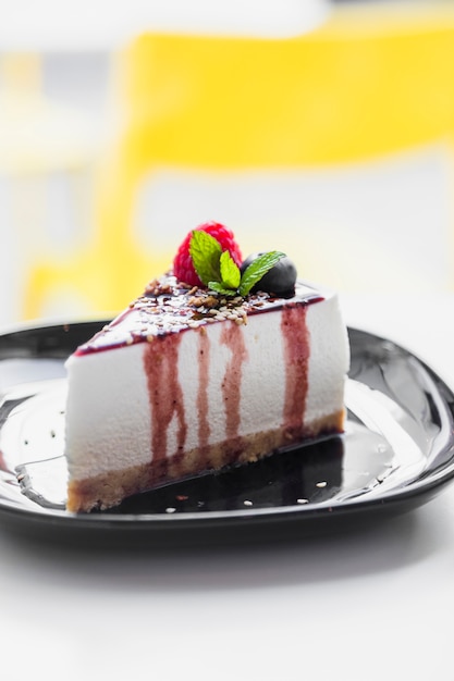 Free photo soft cake topped with raspberry; mint; blueberry & chocolate sauce served on black plate against blur backdrop