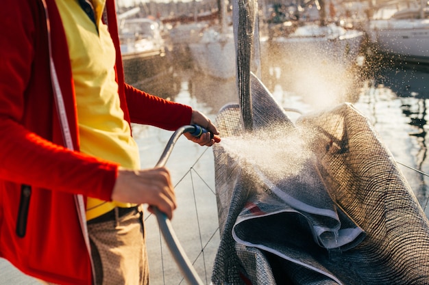 Soft focus of water drops come out of hose, sailor or captain, yacht owner washes salty residue from sail, mainsail or spinnaker, when sailboat is docked in yard or marina