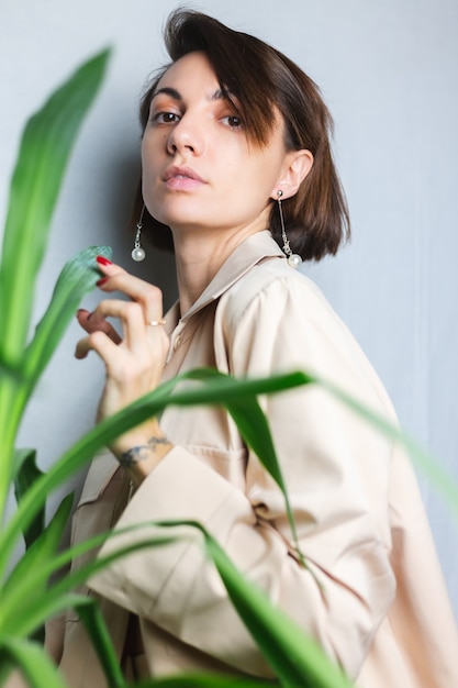 Free photo soft indoor portrait of caucasian gentle woman wearing beige suit no bra, posing behind palm tropical plant,  gray.