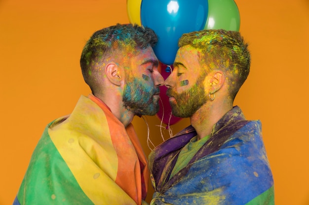 Free photo soiling in paint gay pair gathered kissing wrapped in rainbow flag