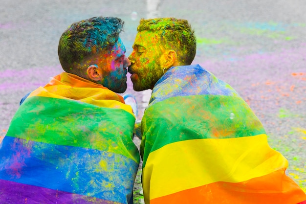 Free photo soiling in paint gay pair kissing wrapped in rainbow flag on lgbt pride parade