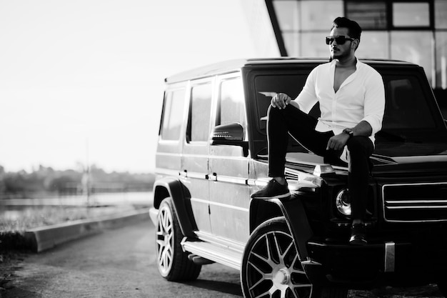 Free Photo solid asian man in white shirt and sunglasses posed near black mafia suv car