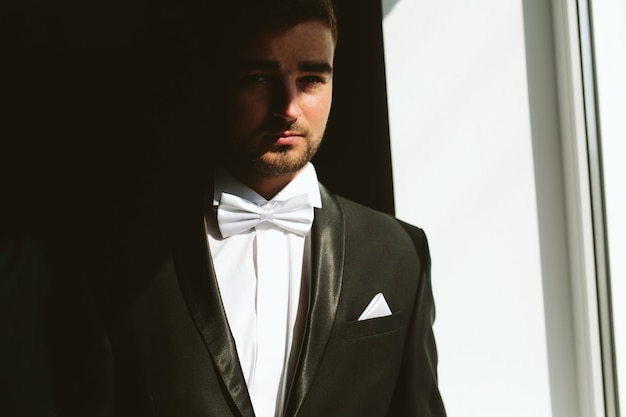 Free photo solid brunette groom in black suit indoor sunlight