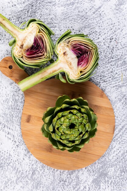 Some artichoke and slices on a cutting board, on light gray background, high angle view.