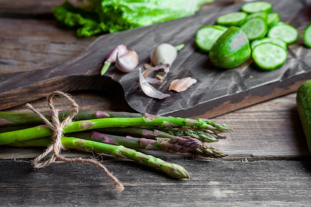 Some asparagus with sliced cucumber, garlic, lettuce in a cutting board on dark wooden background, high angle view.