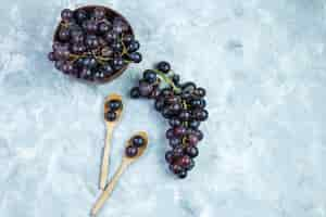 Free photo some black grapes in clay bowl and wooden spoons on grungy grey background, top view.