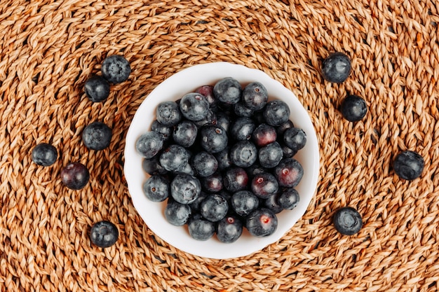 Some black olives in a bowl on rattan trivet background, top view.