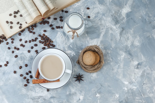 Free photo some coffee with cookies, coffee beans, book, milk, spices in a cup on grey plaster background, top view.