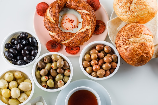 Some eggs with sausage with a cup of tea, turkish bagel, olive, bread in a plate on white surface, top view