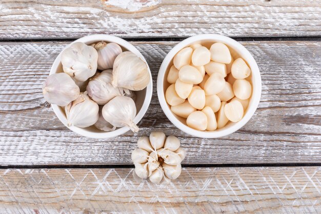 Some garlic in a bowls and nearby on wooden table, top view.