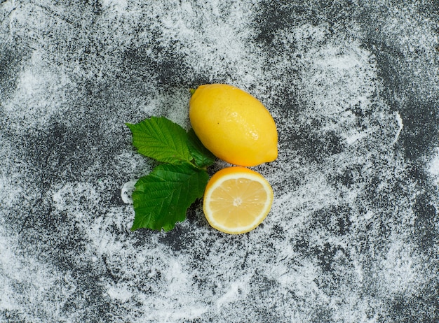 Some lemons with leaves on gray textured surface, top view.