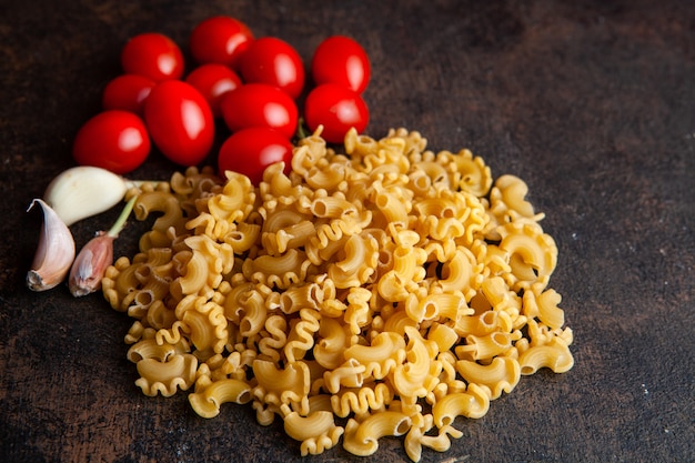 Some macaroni with tomatoes and garlic on dark textured background, high angle view.