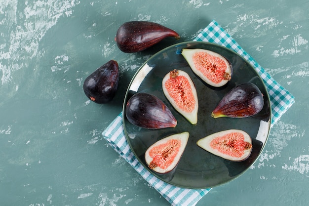 Some mission figs and halves in a bowl and nearby on picnic cloth and teal , flat lay.