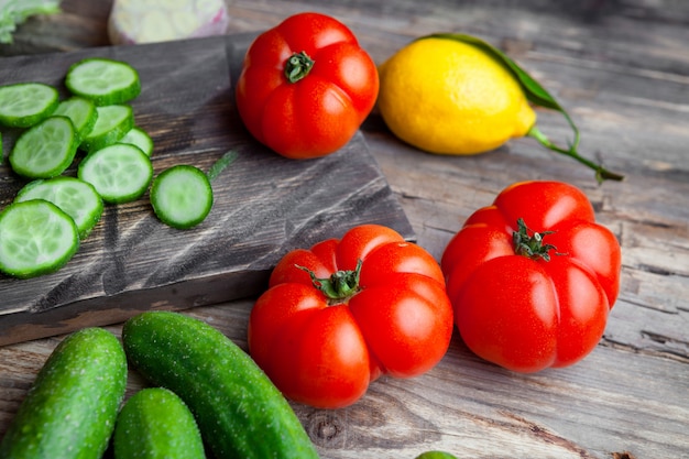 Some sliced cucumber with garlic, tomatoes, lemon in a cutting board on dark wooden background, high angle view