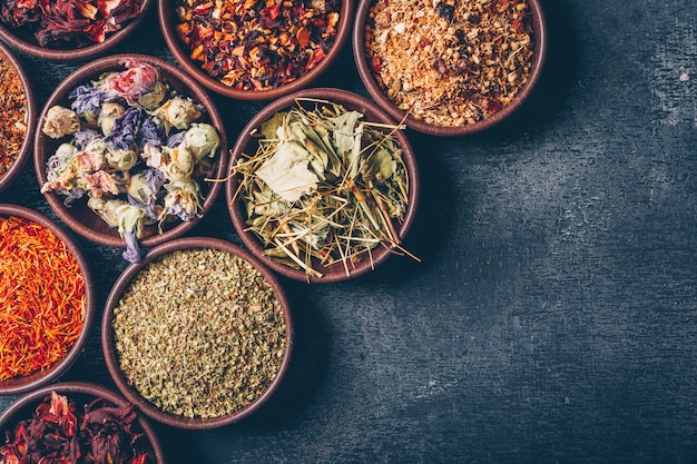 Some tea herbs in a bowls on dark textured background, top view. space for text