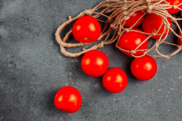 Some tomatoes in a net bag on dark textured background, high angle view.