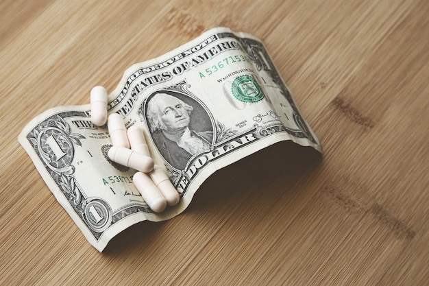 Some white capsules on a dollar bill on a wooden surface