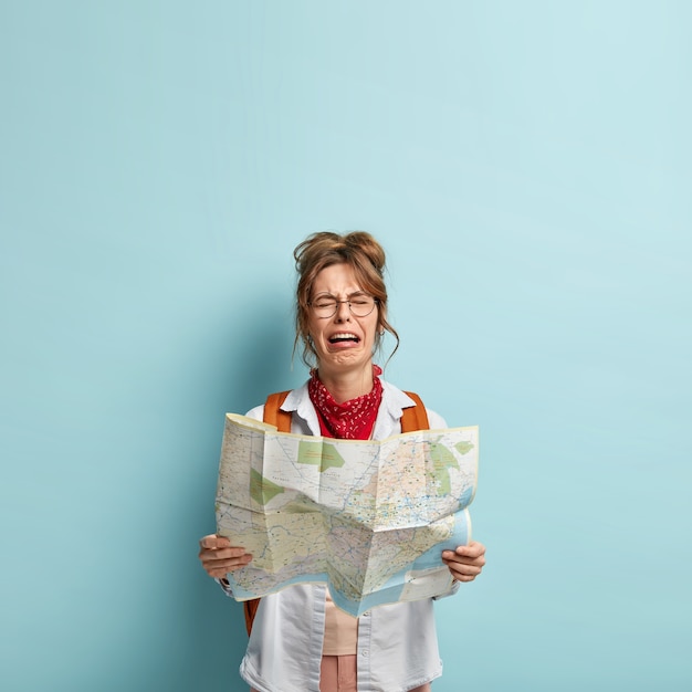 Free photo sorrowful caucasian woman cries from negative feelings, has desperate facial expression, holds tourist map, cannot find right way