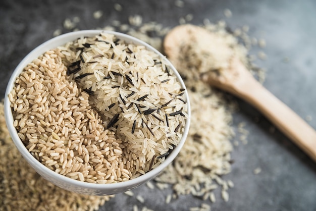 Sorts of rice in bowl near wooden spoon