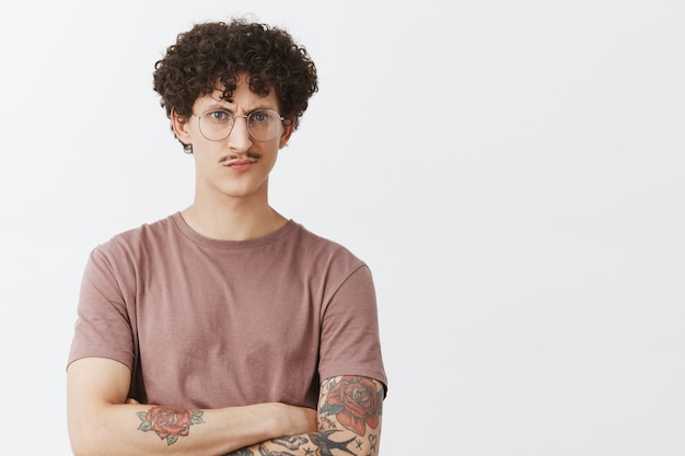 Sounds suspicious and unimpressive. Intense smart and serious-looking young male entrepreneur opening new cafe gazing at business partner with doubt smirking crossing hands on chest, looking concerned