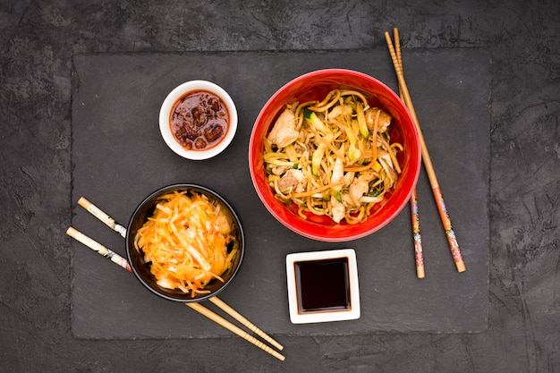 Soy sauce salad and chopstick with tasty chicken noodles on black surface