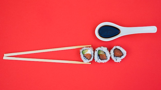 Soya sauce in spoon with chopsticks and sushi on red background