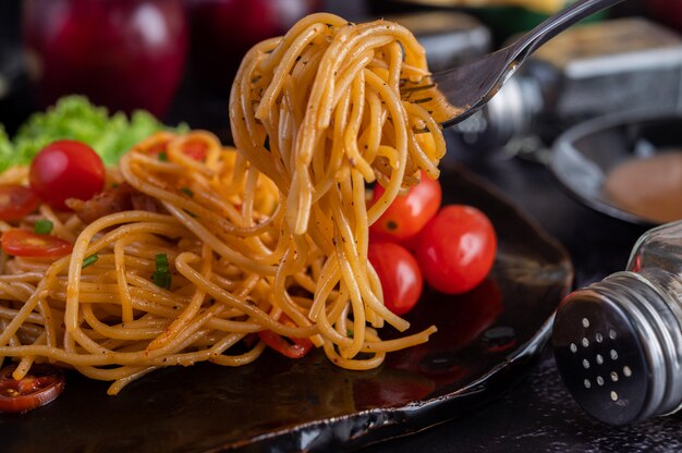 Spaghetti in a black cup with tomatoes and lettuce.