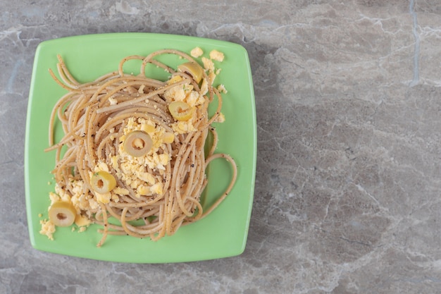 Spaghetti with fried eggs on green plate.