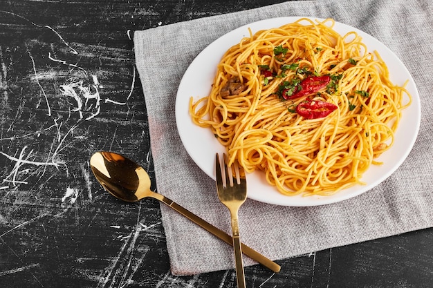 Spaghetti with herbs and vegetables in a white plate, top view