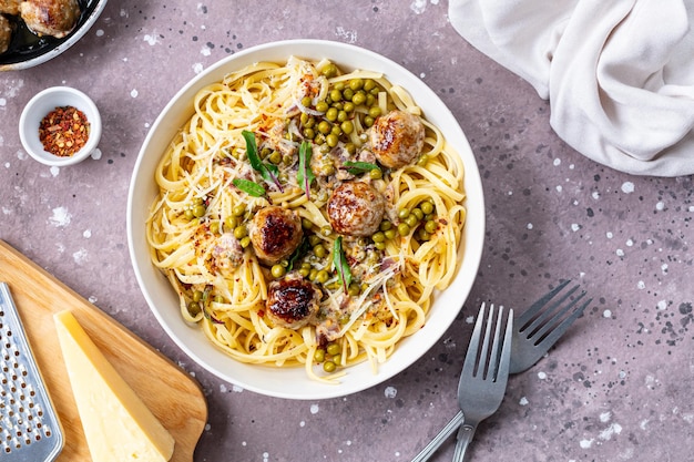 Spaghetti with meatballs and cream sauce is served on a plate with herbs and parmesan