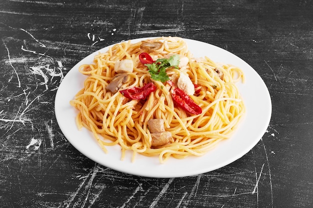 Spaghetti with mixed ingredients in a white plate on black background, top view. 