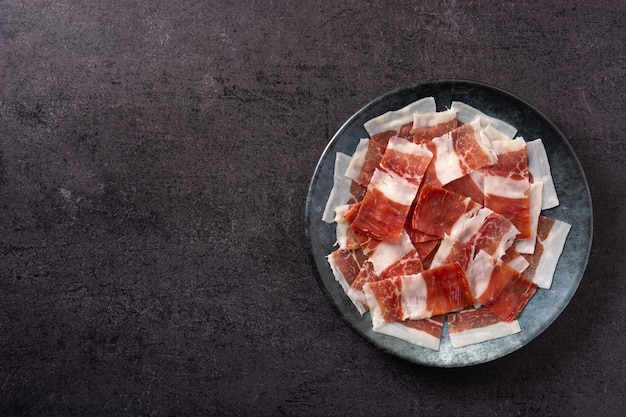 Free photo spanish serrano ham slices on black plate on black slate background