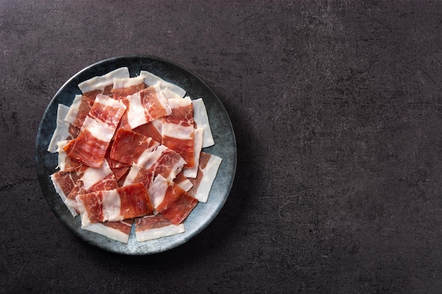 Free photo spanish serrano ham slices on black plate on black slate background