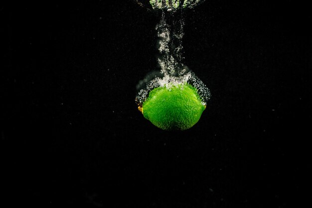 Sparkling green lime splashes water on black background