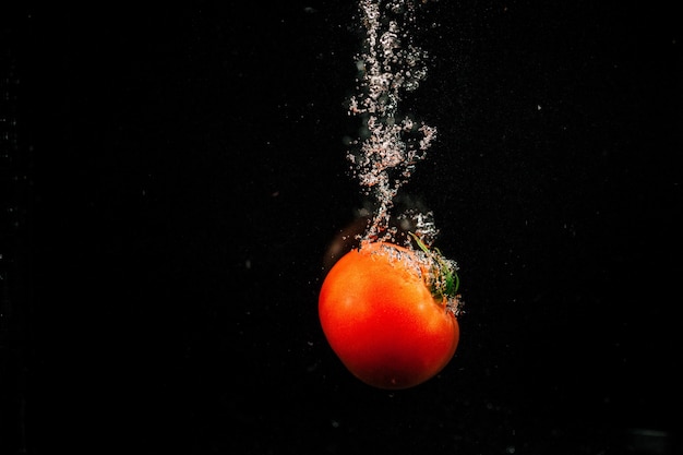 Sparkling red tomato falls in water and splashes it