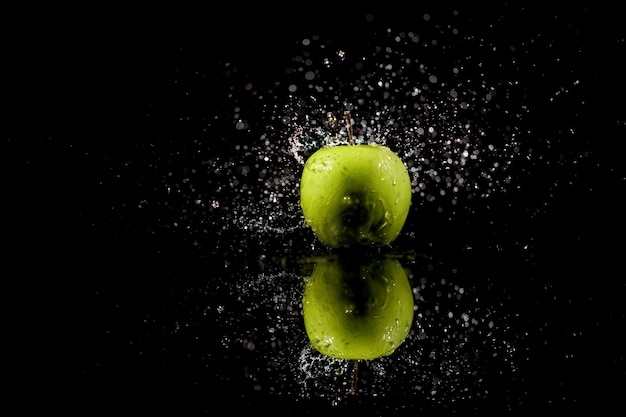 Sparkling water falls on juicy  green apple which stands on black table