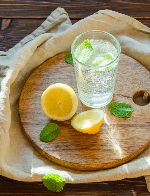 Free photo sparkling water in glass with cutting board, leaves and lemon