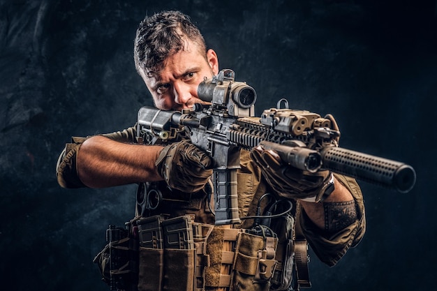 Free Photo special forces soldier wearing body armor holding assault rifle and aim at the enemy. studio photo against a dark textured wall