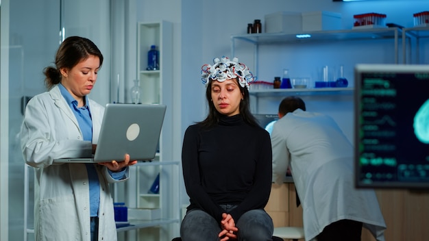 Specialist neurologist doctor taking notes on laptop asking patient's symptoms adjusting high tech eeg headset