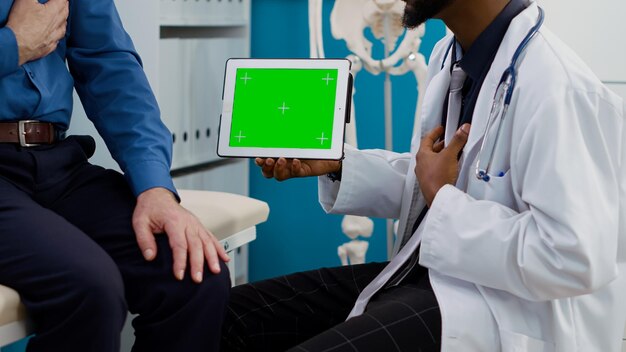 Specialist showing horizontal greenscreen on tablet to senior patient, looking at chromakey display. Old person and physician using blank mockup template with copyspace background. Close up.