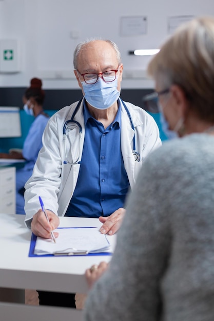 Free photo specialist taking notes on clipboard papers while doing consultation with woman during covid 19 pandemic. man doctor preparing prescription document for treatment against disease.