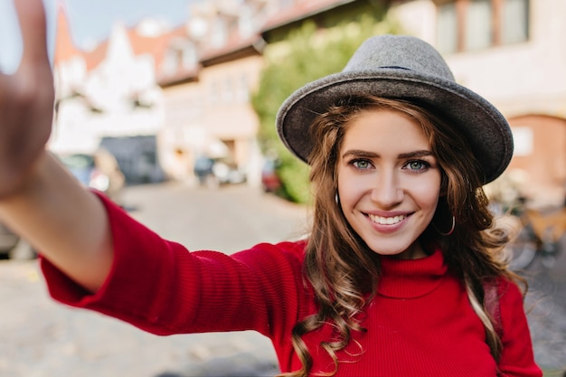 Free photo spectacular blue-eyed white woman in elegant hat making selfie with blissful smile