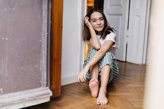 Free photo spectacular female model in pajamas chilling at home. indoor photo of joyful brunette girl posing on the floor.