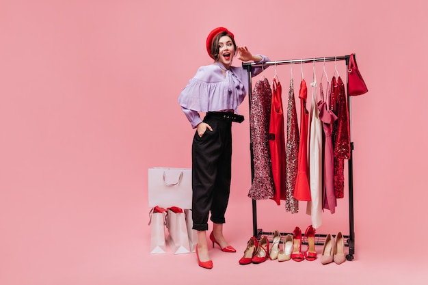 Free photo spectacular lady in black pants coquettishly lifts her leg and holds bag on pink background with packages after shopping.