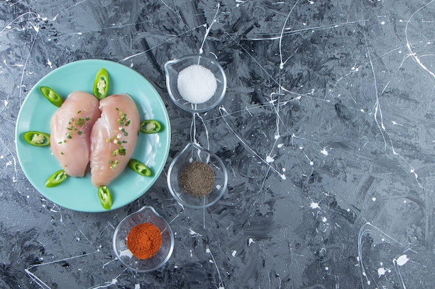 Free Photo spice bowls and chicken breast on a plate , on the marble background. 