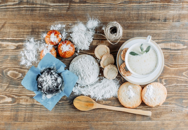 Spicy milk in a cup with biscuits, spoon, rope, powdered sugar top view on a wooden surface