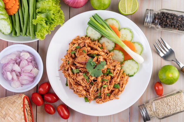 Spicy minced chicken on a white plate complete with cucumber, lettuce and side dishes.