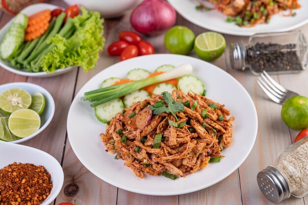 Spicy minced chicken on a white plate complete with cucumber, lettuce and side dishes.