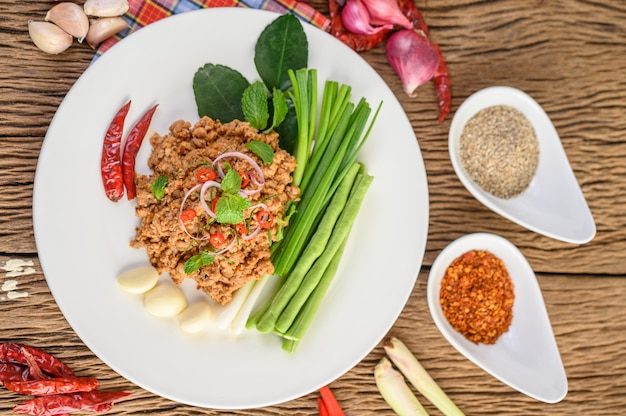 Spicy Minced Pork Salad on a white plate with red onion, lemon grass, garlic, yardlong beans, kaffir lime leaves, and spring onion